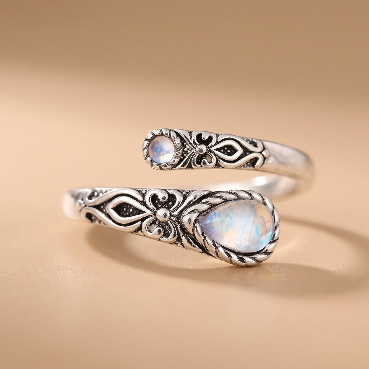 hero: A NEW photorealistic photograph composed from scratch. The ring is placed on a seamless matte warm beige studio surface that smoothly transitions into a matching, softly graduated background. One large soft diffused light source from camera left provides gentle frontal fill, creating controlled highlights on the metal and gemstones, soft tonal transitions, and a subtle realistic contact shadow directly beneath the product. The scene is captured with a straight-on eye-level product view using a macro…
