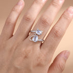 lifestyle: A NEW photorealistic photograph composed from scratch. The product is worn on the ring finger, its design clearly visible and facing outwards. The back of a relaxed adult hand is positioned diagonally across the frame, with fingers naturally and gently separated, against a seamless matte warm beige studio surface that blends into a softly graduated warm beige background. Camera is eye-level, using an 85mm portrait lens with a shallow depth of field (f/2.8) to softly blur the background. Soft dif…
